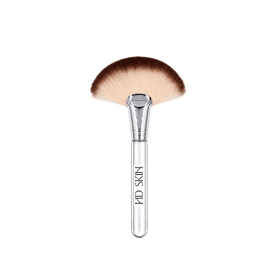 The Fluff Brush facial cleansing brush with a clear handle and fan-shaped soft bristles in gradient brown and cream tones